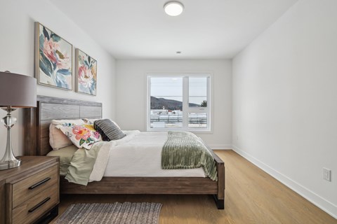 A bedroom with a bed, nightstand, and a window overlooking the water.