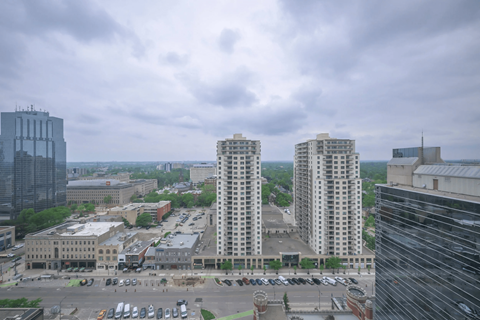 A cityscape with a mix of modern and older buildings, a parking lot, and a cloudy sky.