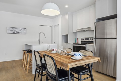 A modern kitchen with a wooden table and chairs, a stainless steel refrigerator, and a quote on the wall.