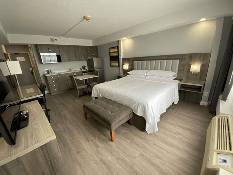 A bedroom with a bed, nightstand, and a small kitchenette.