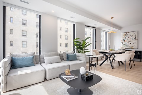 A modern living room with a white sofa, a black coffee table, and a dining table with chairs.