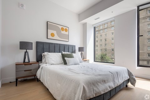 A bedroom with a large bed and a city view window.