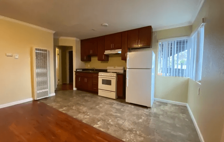 an empty kitchen with white appliances and wooden floors