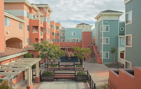 A courtyard surrounded by buildings with a black fence and a tree.