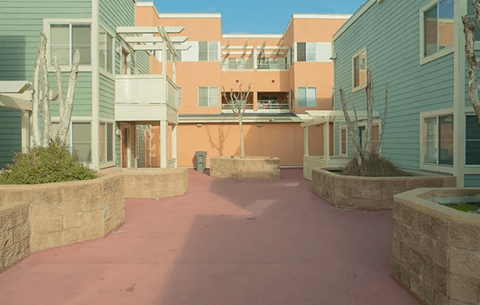 A courtyard surrounded by buildings with a pinkish ground.