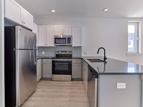 A modern kitchen with a stainless steel refrigerator and a black countertop.