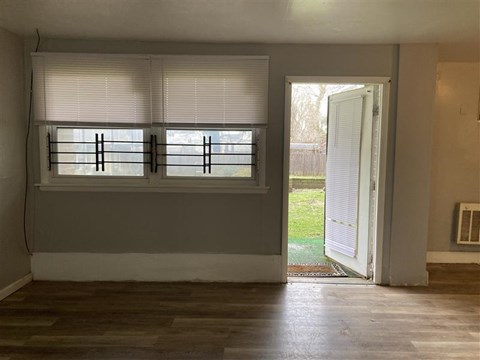 A room with a window covered by white blinds and a door open to a backyard.