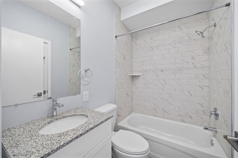 A white bathroom with a marble counter top and a white bathtub.