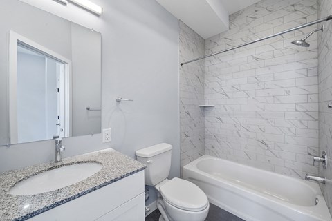 A white bathroom with a marble counter top and a white tub.