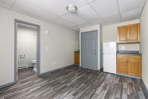 the living room and kitchen of an apartment with a refrigerator and a sink