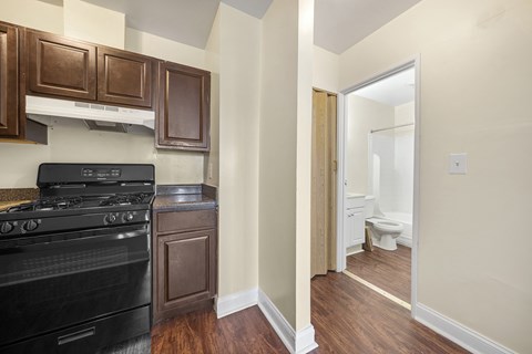 a kitchen with black appliances and wood flooring and a door to the bathroom