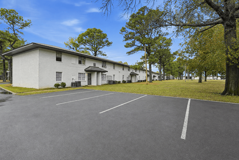 A parking lot in front of a white building with trees on the side.