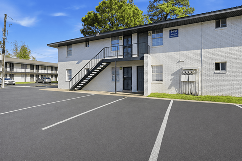 A parking lot in front of a white building with a black staircase.