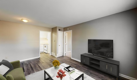 A living room with a green chair, a coffee table with a vase of flowers, and a television on a cabinet.