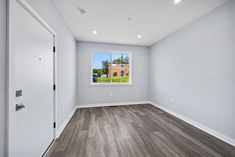A room with a white door and a window showing a building outside.