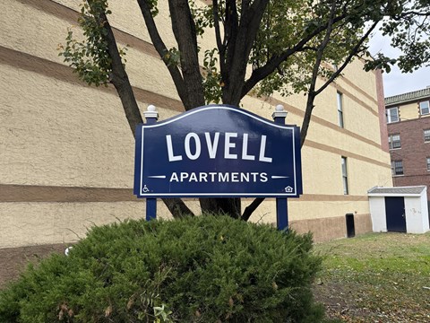 A blue sign that says Lovell Apartments stands in front of a building.