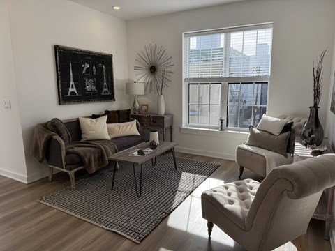 A living room with a grey couch, a coffee table, and a large window.