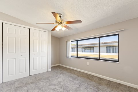 A room with a ceiling fan and a window overlooking a building.