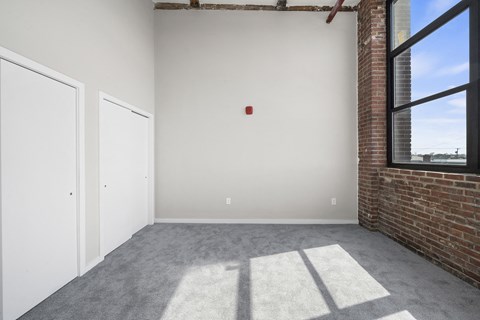 A room with a white door and a window with a brick wall.