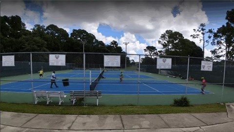 A tennis court with people playing tennis and a cloudy sky.