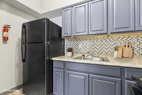 A black refrigerator in a kitchen with blue cabinets.