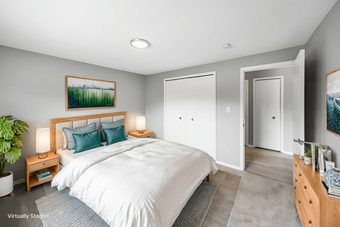 A bedroom with a large bed, a nightstand with a lamp, and a painting on the wall.