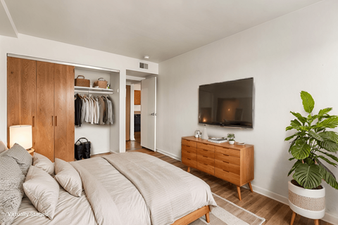 A bedroom with a large bed, a wooden wardrobe, and a TV mounted on the wall.