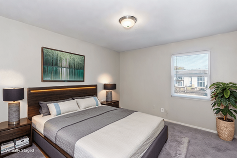A bedroom with a large bed, two lamps, a painting, and a potted plant.
