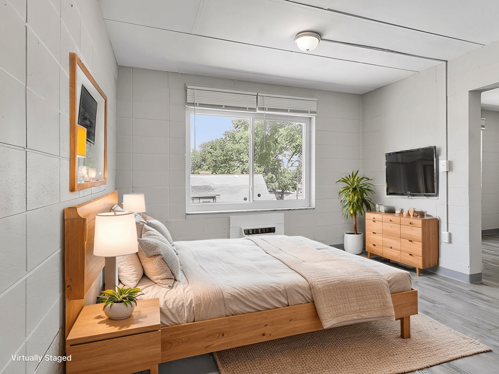 A bedroom with a bed, nightstand, and a window with a view of trees.