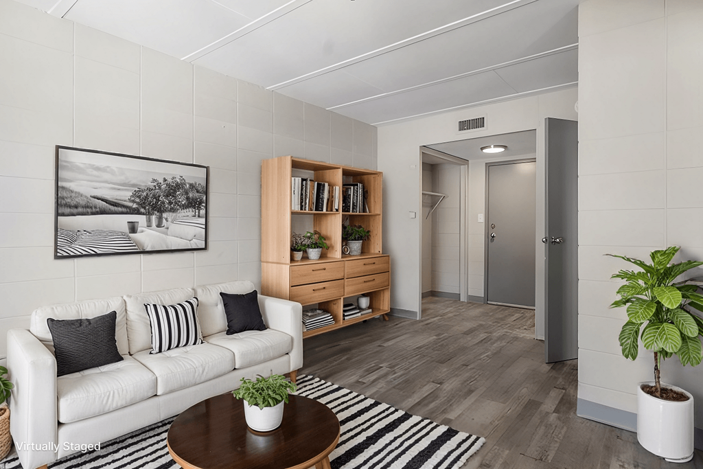 A living room with a white couch, a coffee table, a bookshelf, and a potted plant.