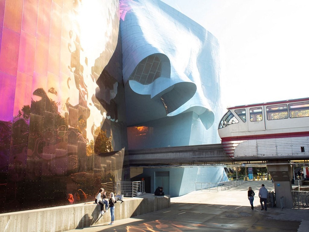 people walking in front of a building with a train on a bridge