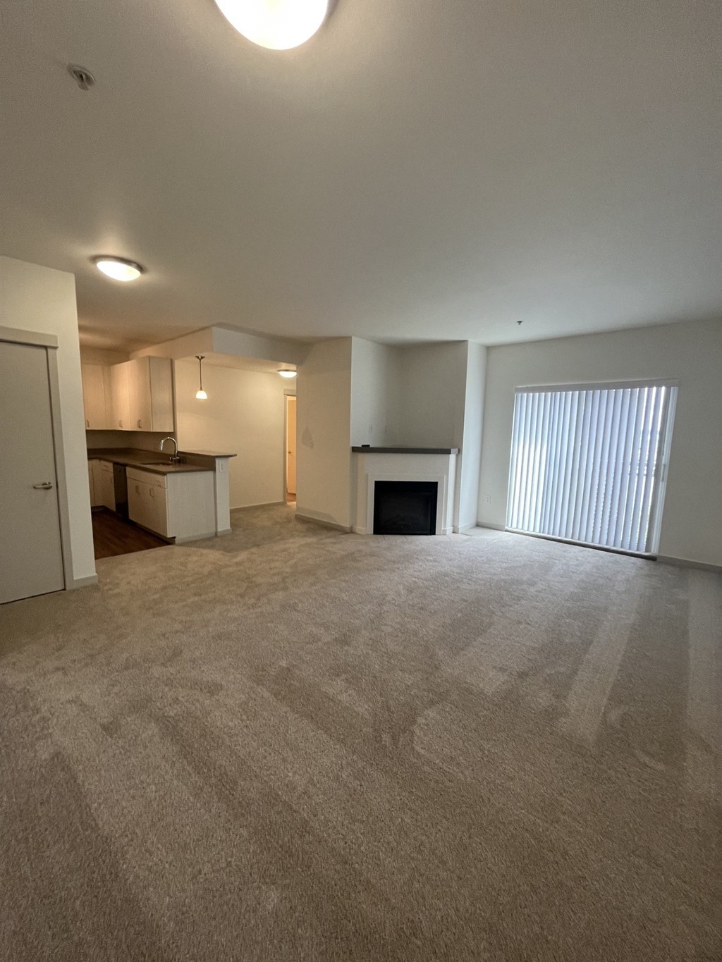 an empty living room with a fireplace and a kitchen
