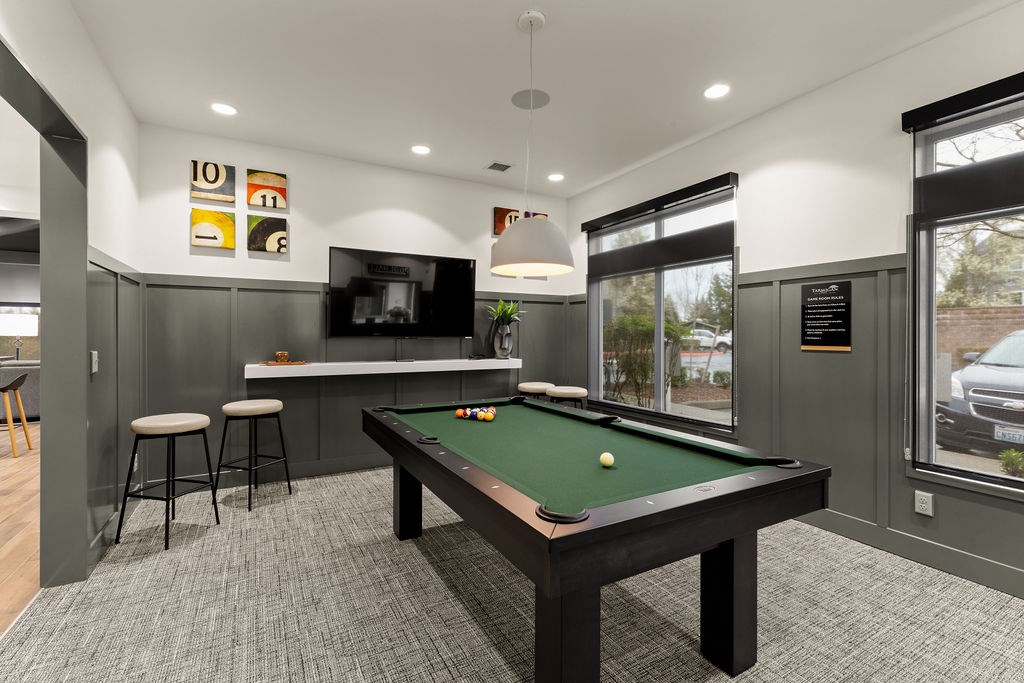 A pool table is in the middle of a room with a bar and stools.