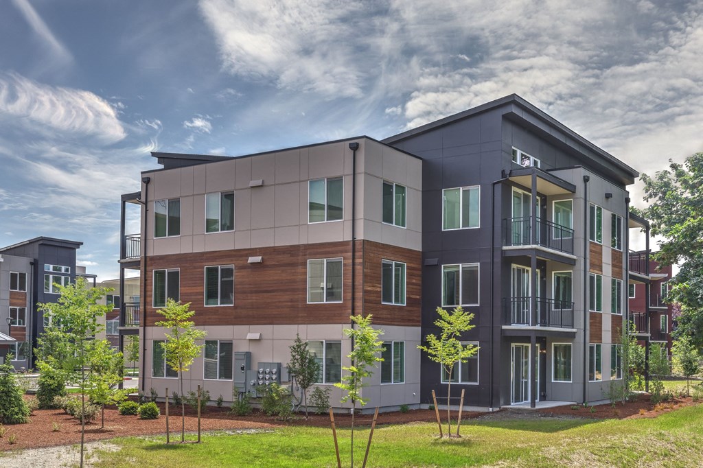 a modern apartment building with green grass and a cloudy sky