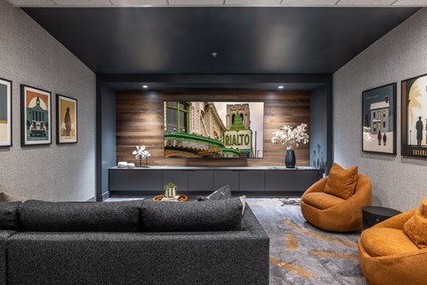 A living room with a grey couch and a large painting of a green landscape.