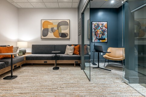 A modern office space with a grey sofa, orange pillows, and a glass wall.