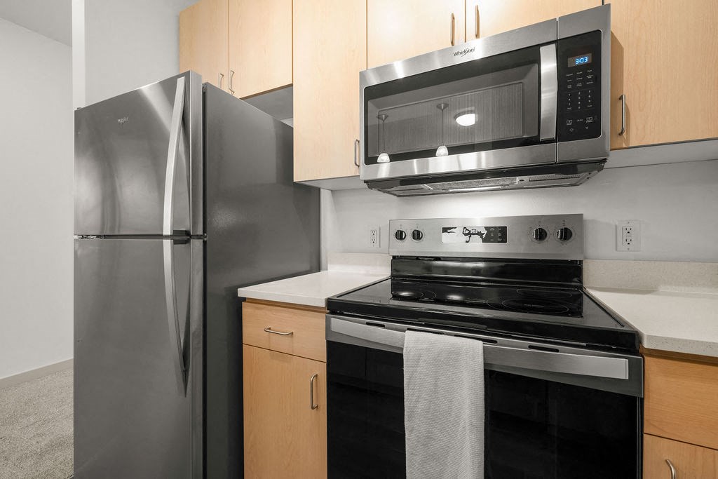 A kitchen with a stainless steel refrigerator, black stove, and microwave above it.