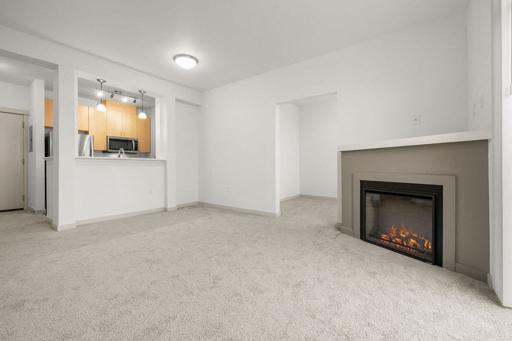A living room with a fireplace and a kitchen area in the background.