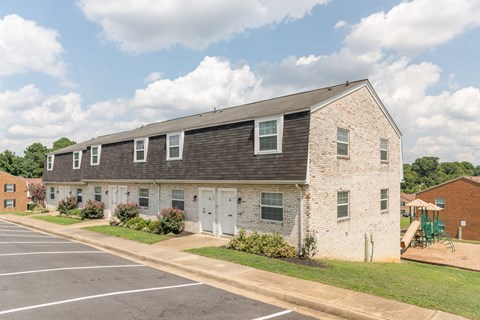 A white brick building with a black roof and a parking lot in front.
