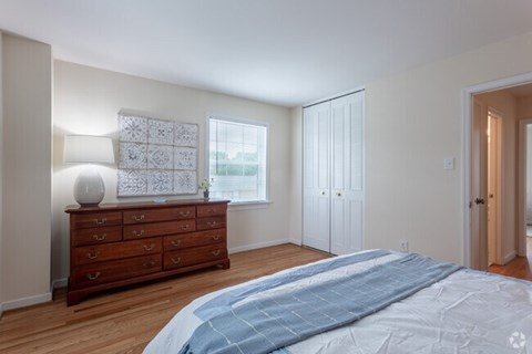 A bedroom with a large bed and a dresser with a lamp on it.