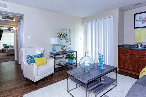 A living room with a white chair and a glass table with a blue vase on it.