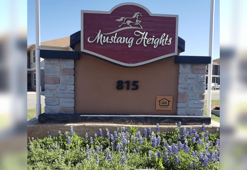 Mustang Heights sign with a stone pillar and flowers in the foreground.