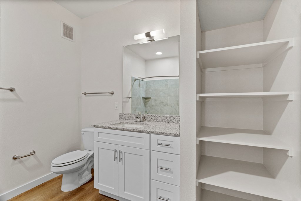 A white bathroom with a toilet, sink, and shelves at SOSA at Palo Alto Apartments, San Antonio, Texas