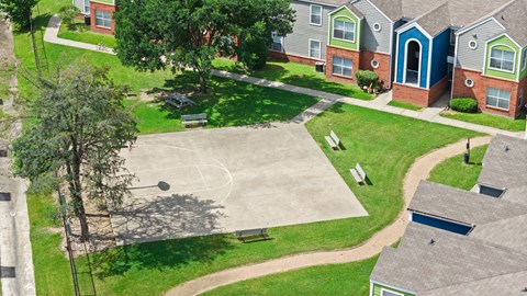 A basketball court is surrounded by houses and trees.