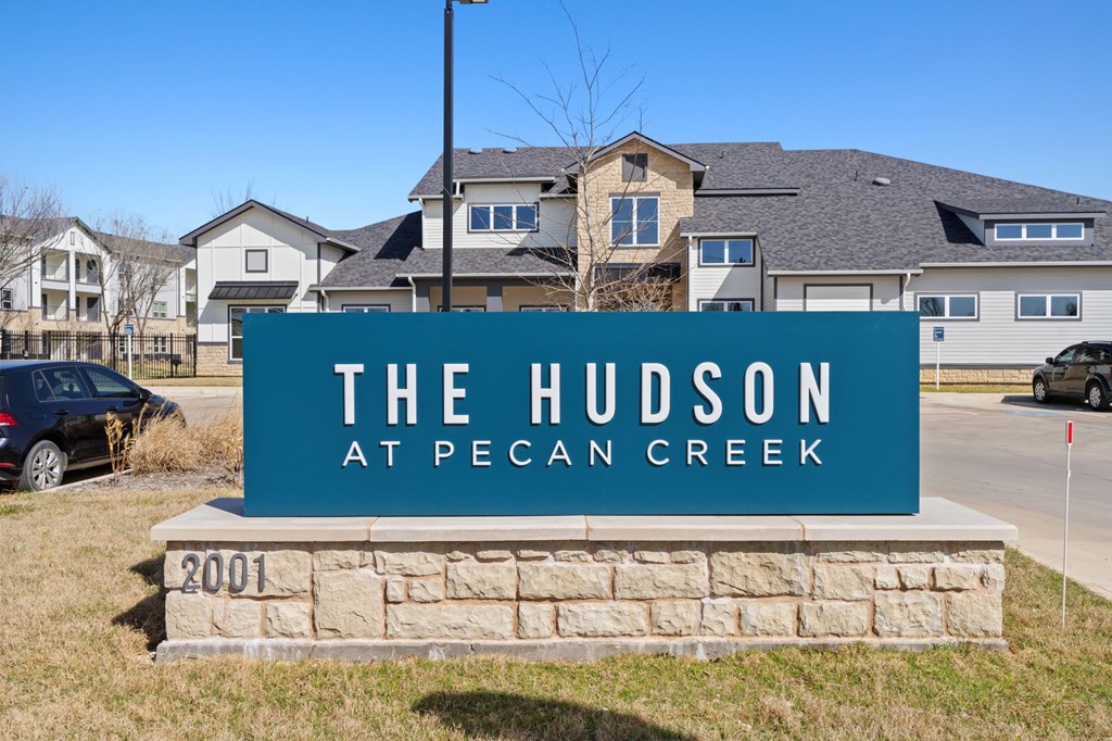 A sign for The Hudson at Pecan Creek is in front of a building.
