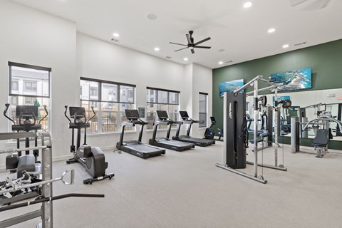 A spacious gym with a variety of equipment including treadmills, elliptical machines, and weight machines. at Hudson at Pecan Creek Apartments, Denton 76205