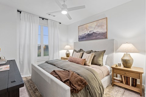 A bedroom with a large bed, a ceiling fan, and a painting on the wall.