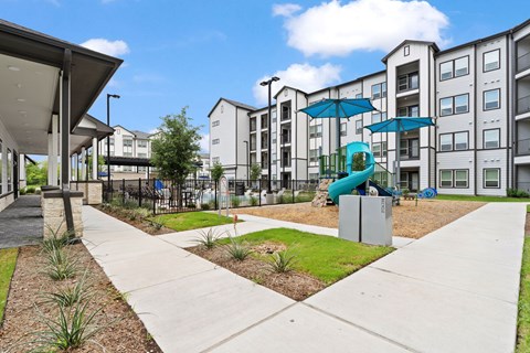 Playground area with shade structures and apartment buildings at Tapestry Orem Apartments, Houston