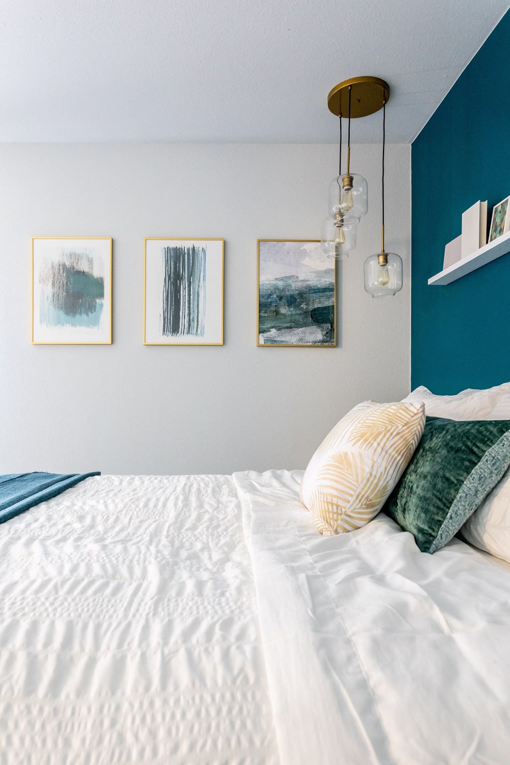 a bed with white sheets and green pillows and pictures on the wall above it