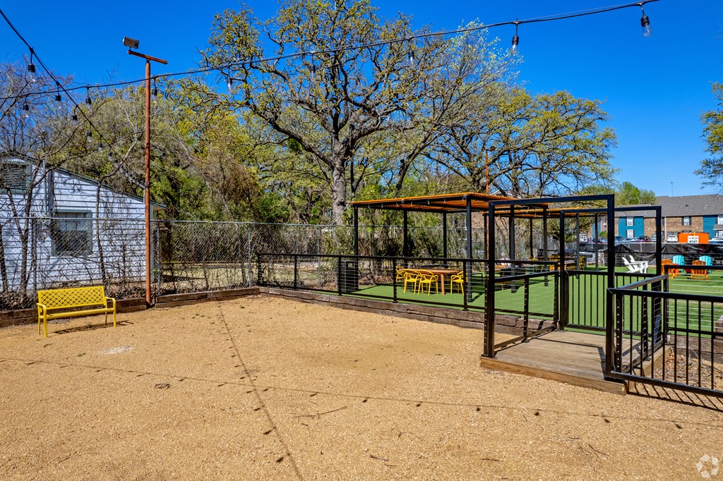 a fenced in dog park with a yellow bench and gazebo